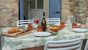 Un espacio de comedor al aire libre con un muro de piedra, una puerta azul y una mesa dispuesta con platos, vasos y una botella.