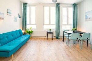 Quarto com sofá verde-água, uma mesa de jantar com cadeiras, uma mesinha lateral e um radiador.