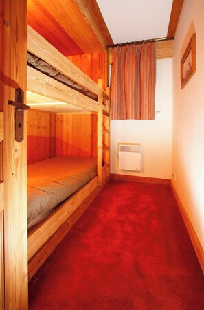 A bunk bed room with a red carpet, wooden walls, a window with curtains, and a wall-mounted heater. - Alpine Apartment for a Family of 6 (Les Deux Alpes)
