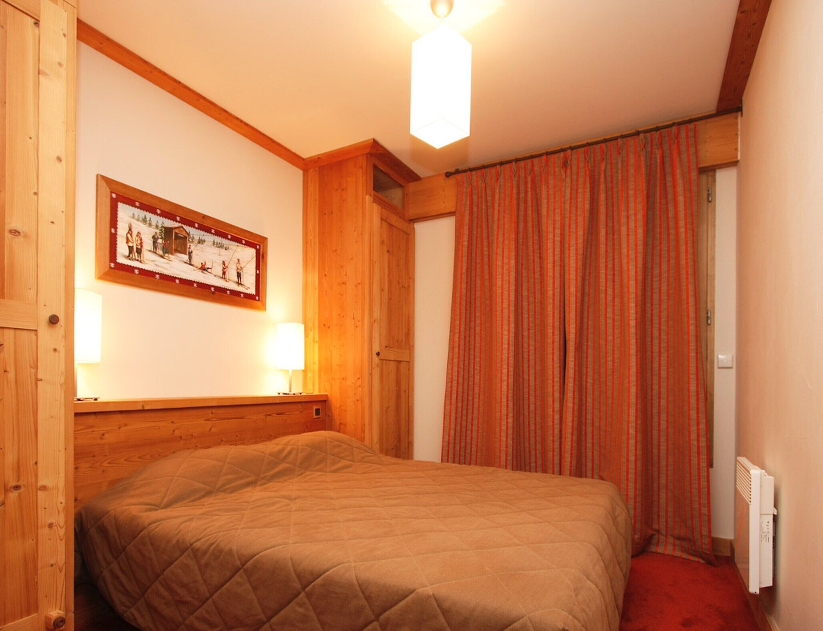 Ein Schlafzimmer mit einem Holz-Kopfteil, einer gesteppten Bettdecke, einem gerahmten Bild an der Wand und einem Fenster mit Vorhängen.