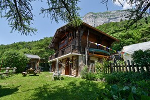 A wooden chalet with a balcony, surrounded by lush greenery and a mountain backdrop. - La Télécabine Guest Room (La Balme-de-Thuy)
