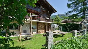 A wooden chalet with a balcony, a stone wall, and a garden area with a bench. - La Télécabine Guest Room (La Balme-de-Thuy)