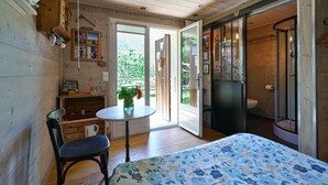 A wooden cabin with a bed, a table with a chair, a small kitchenette, and a bathroom with a shower. - La Télécabine Guest Room (La Balme-de-Thuy)