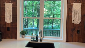 Una cucina con un lavello doppio, pareti rivestite in legno, una finestra vista alberi e decorazioni a macramè.
