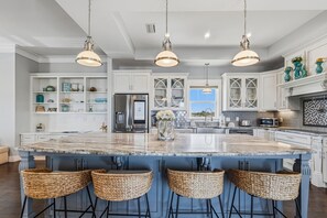 A kitchen with a large island, white cabinets, and hanging pendant lights.