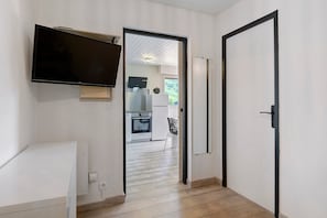 A hallway with a TV mounted on the wall, a door, and a view into a kitchen area.