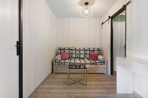 Un corridoio stretto con una porta scorrevole, un divano con cuscini decorati e un tavolino.