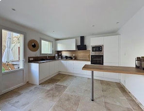 A modern kitchen with white cabinetry, a wooden countertop, a built-in oven, and a window.