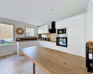 Une cuisine moderne avec des meubles blancs, un plan de travail en bois et des appareils électroménagers intégrés, notamment un four à micro-ondes et un four traditionnel.