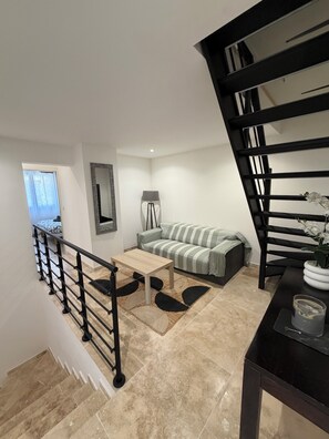 A modern living room with a sofa, a coffee table, a lamp, and a staircase.