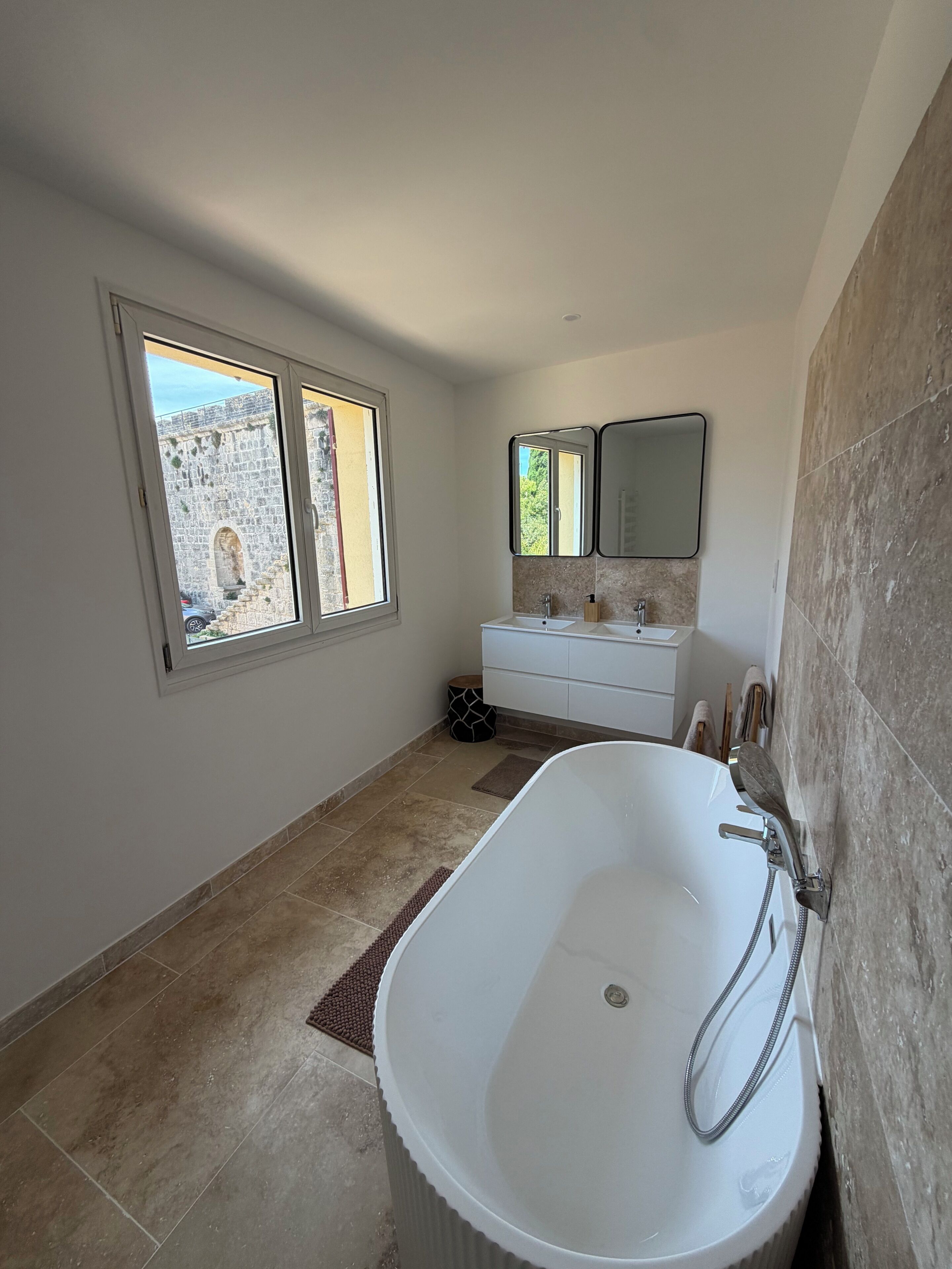 Un baño moderno con una bañera independiente, un lavamanos doble y un ventanal grande.
