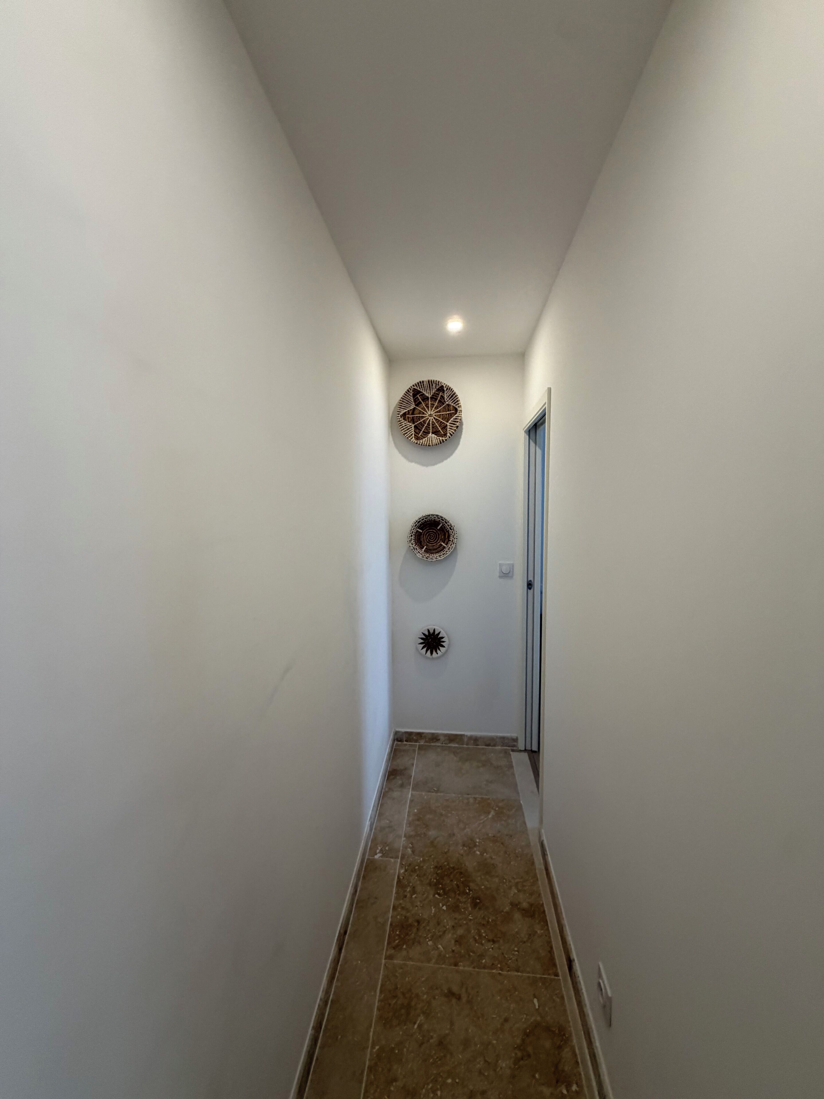 Un couloir étroit aux murs blancs et au sol carrelé.