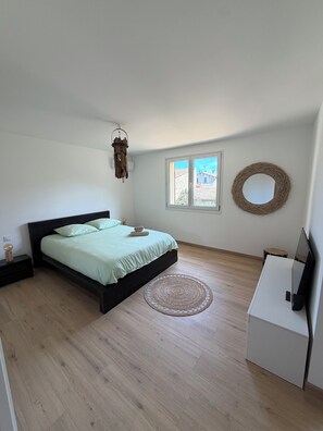 Une chambre à coucher avec un lit, un miroir rond, une petite table ronde, un téléviseur et une fenêtre donnant sur des immeubles.