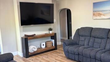 Un salon moderne doté d’un téléviseur à écran plat, d’un meuble de rangement en bois et de deux canapés gris.