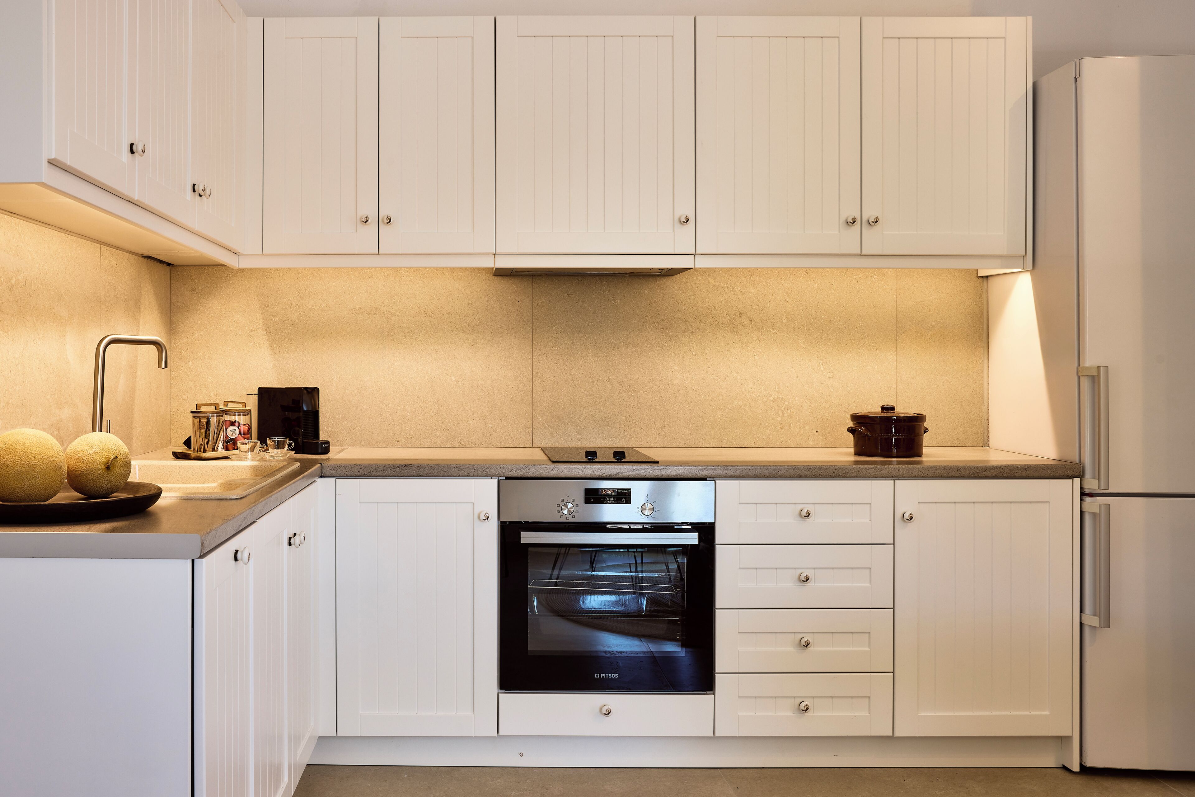 A modern kitchen with white cabinetry, a built-in oven, and a refrigerator.