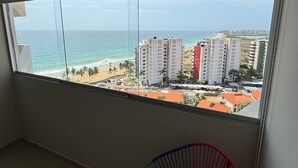 Una habitación con un amplio ventanal con vistas a la playa, un abanico decorativo y suelo de baldosas.