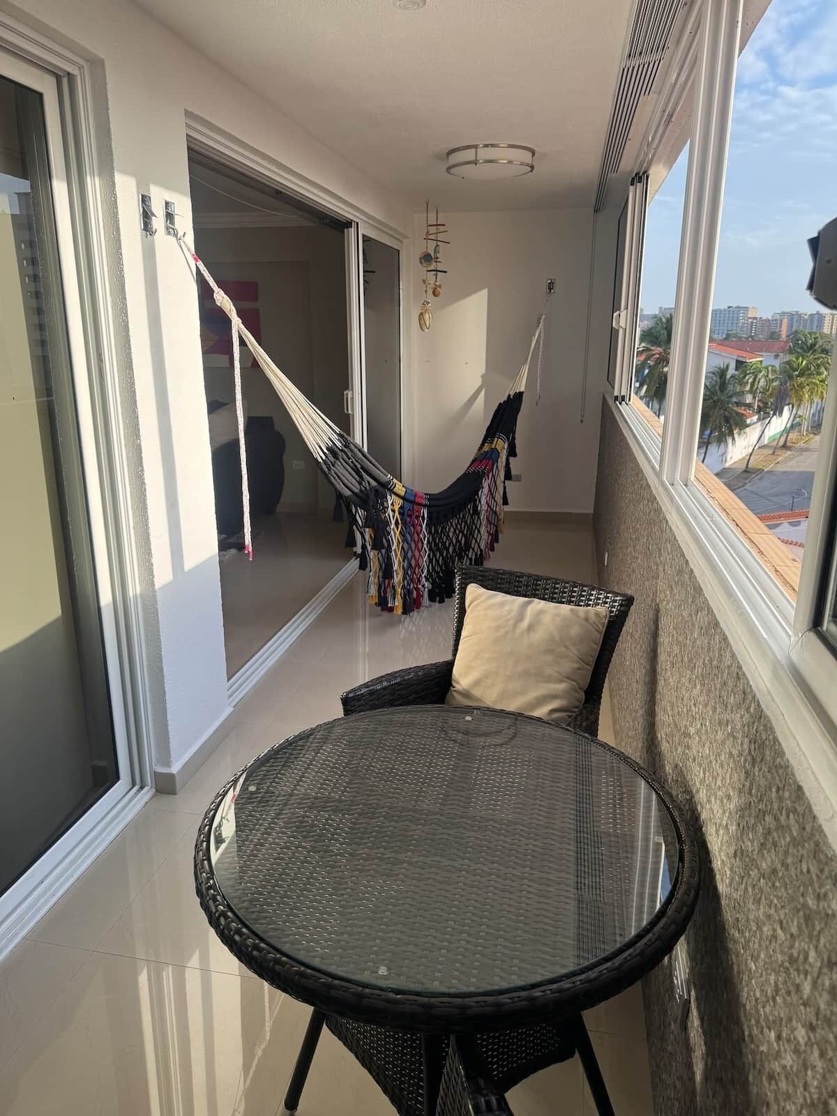 Un balcon avec une table en osier, un hamac et une vue sur la ville.