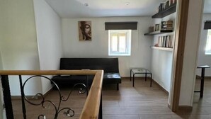 A spacious living area with a sofa, a small table, a bookshelf, and a window.