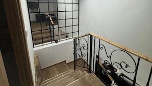 A staircase with wooden steps and a metal railing, leading to a room with a white wall and a window with a grid pattern.