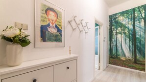 A hallway with a white console, a framed poster, a vase with flowers, and a forest mural on the wall. - Cool stay at 2 steps from Duomo, Como (Como)