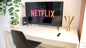 A modern office desk with a flat-screen TV displaying 'NETFLIX' in bold letters, a potted plant, a remote control, and a decorative vase with sticks. - Cool stay at 2 steps from Duomo, Como (Como)