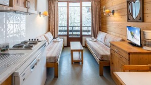 A compact cabin with a kitchenette, a sofa bed, a small table, and a television. - Slope-access Morillon Apartment for 4 (Morillon)