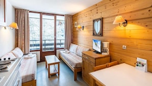 A cozy cabin-style room with a sofa, a small table, a TV, and a coffee maker. - Slope-access Morillon Apartment for 4 (Morillon)