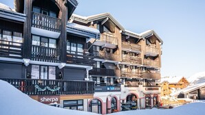 A multi-story hotel with balconies, ski rental signage, and a Sherpa store. - Slope-access Morillon Apartment for 4 (Morillon)