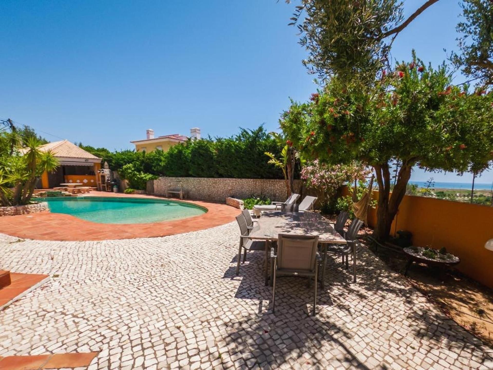 A pool area with a tiled deck, lounge chairs, and a view of the sea.