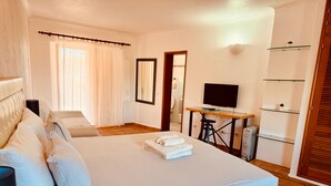 A bedroom with a bed, a desk, a TV, and a bathroom visible through an open door. - Studio Apartment With Pool Meia Praia Beach, Lagos (Lagos)