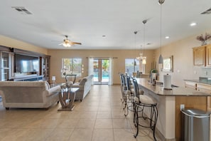 A spacious living area with a sofa, a dining table with chairs, a kitchen with a bar, and a ceiling fan.
