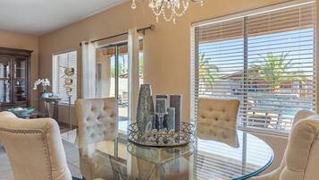 Un espace repas avec une table en verre, des chaises rembourrées, un lustre et une vue dégagée grâce à de grandes fenêtres.