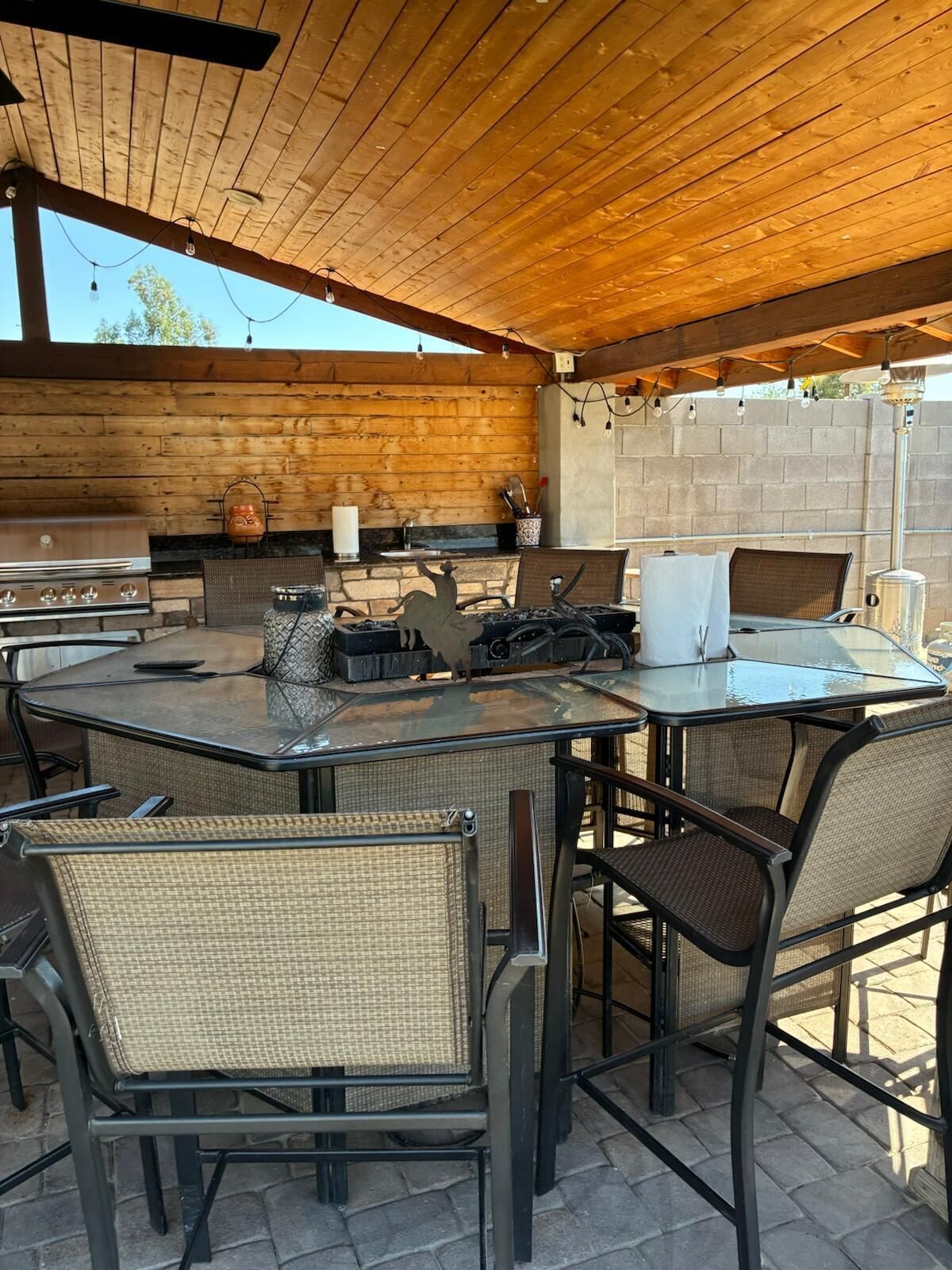 Une terrasse extérieure dotée d’un plafond en bois, d’un barbecue, de chaises en osier et d’une table en verre.