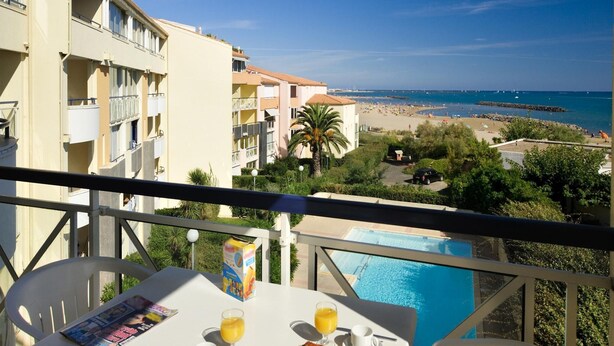 Un balcón con una mesa lista para el desayuno, con vistas a una playa y una piscina.