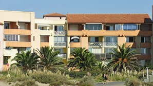 Un hotel de varios pisos con balcones, palmeras y un primer plano de arena.