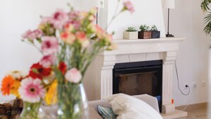 A living room with a fireplace, a sofa, a coffee table with a vase of flowers, and a lamp. - Luxury Villa on Prata Costa With Private Pool, Terrace With Lagoon View (Caldas da Rainha)