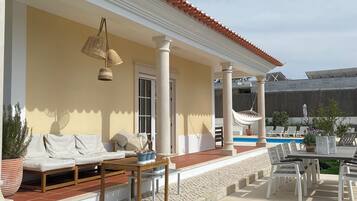 A covered outdoor area with a pool, white columns, and a seating area with cushions.