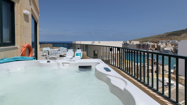 Zona de piscina en la azotea con hidromasaje, sillas de descanso y vistas al mar y edificios.