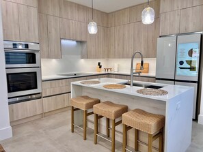 Eine moderne Küche mit Holzausstattung, Edelstahlgeräten, einer weißen Kochinsel mit Hockern und Pendelleuchten.
