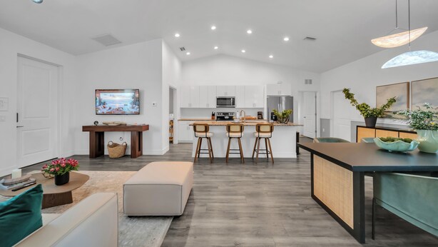A modern kitchen with a central island, bar stools, and a dining area with a table and chairs. - Emerald Entry Retreat (LaBelle)