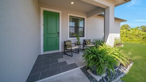 A house with a green door, a window with blinds, a porch with chairs, and a potted plant. - Emerald Entry Retreat (LaBelle)