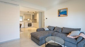 A modern living room with a grey sectional sofa, a glass coffee table, and a kitchen in the background. - #1 Holiday Apartment MTG - Orebić (Orebić)