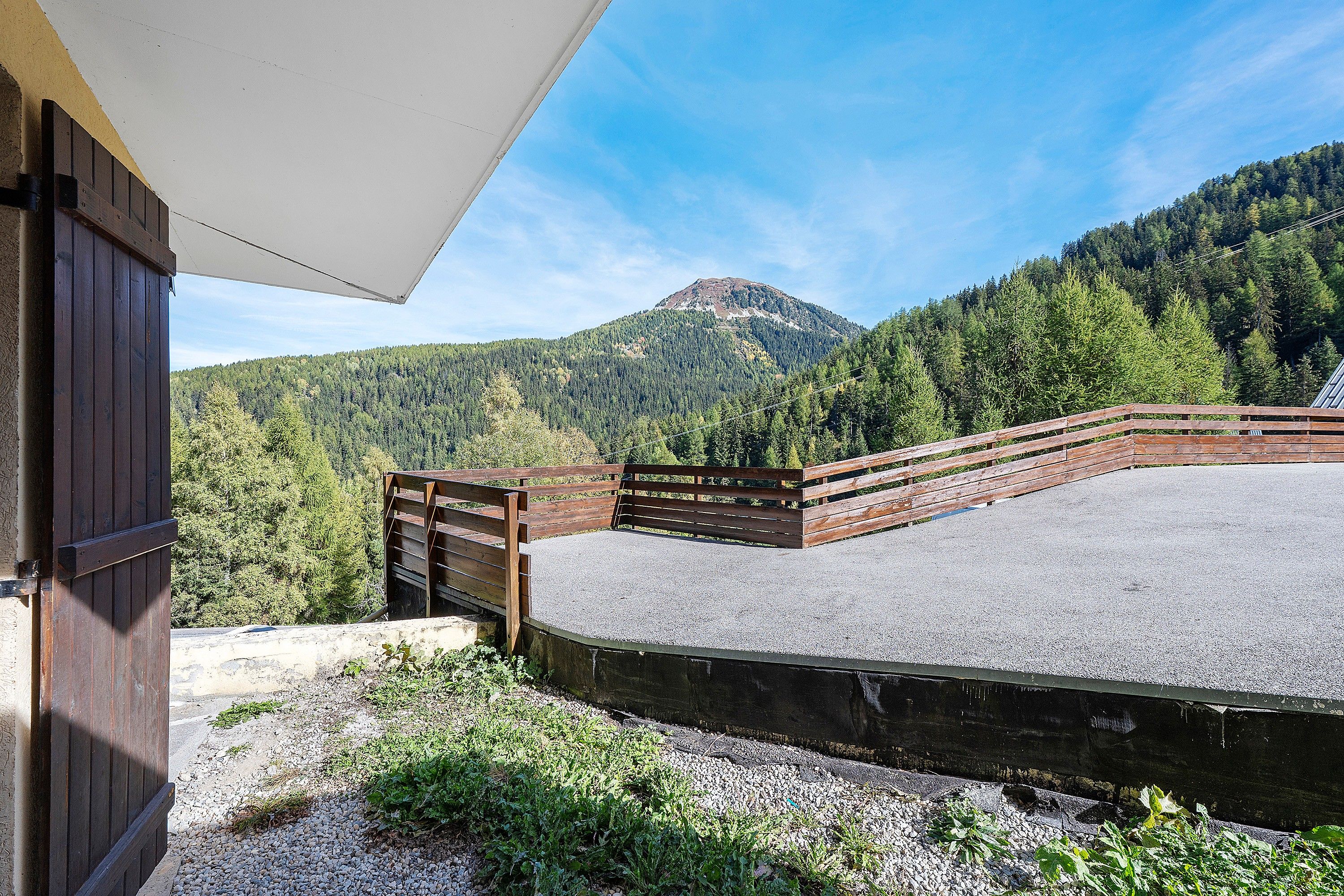 Une terrasse en gravier, avec une clôture en bois et une vue sur les montagnes en arrière-plan.