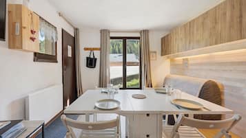 Un coin repas avec une table dressée pour deux personnes, un buffet en bois orné d’un motif en forme de cœur, et une vue sur une forêt par la fenêtre.