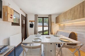 Un comedor con una mesa lista para dos, un mueble de madera con un adorno en forma de corazón y vistas a un bosque a través de una ventana.