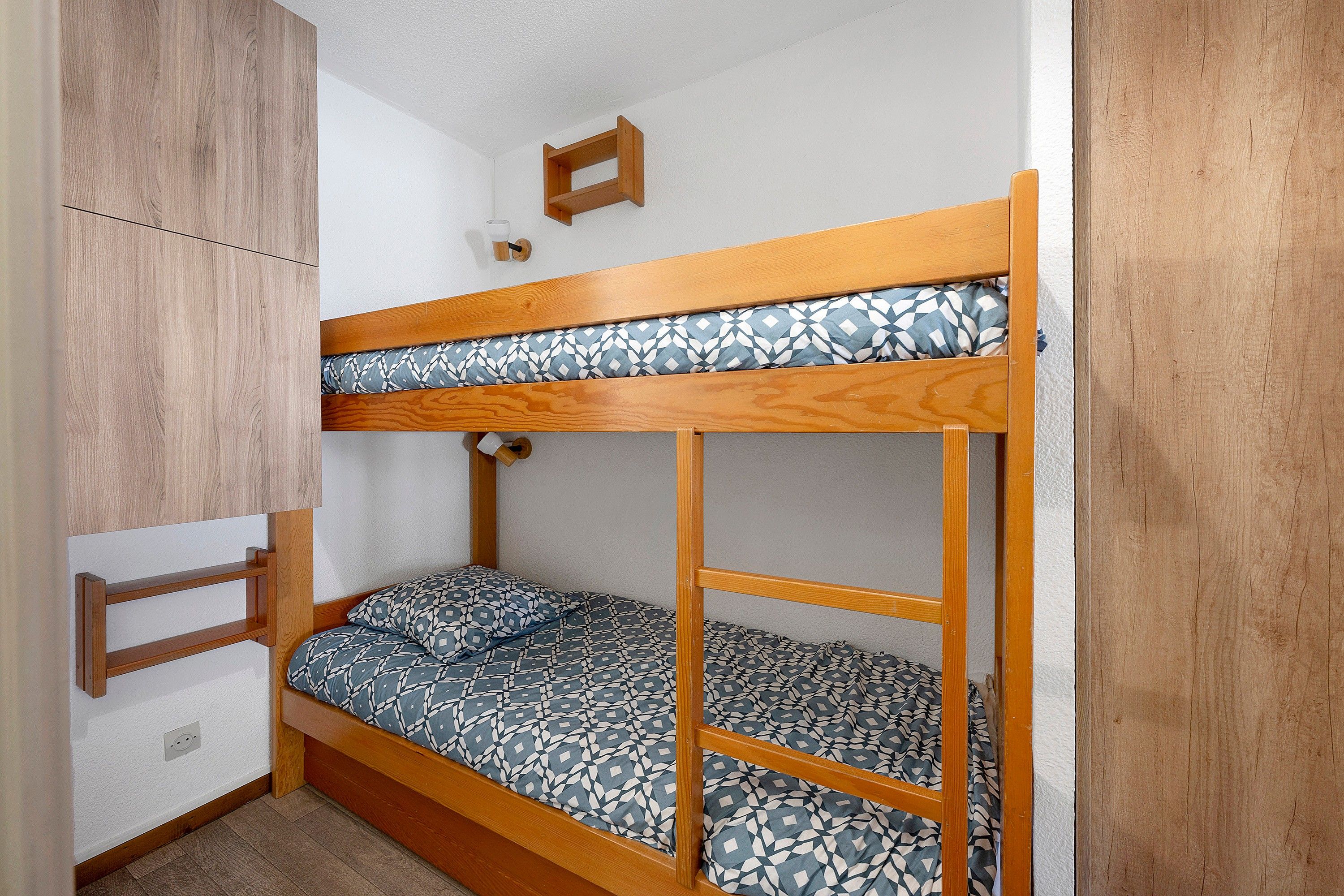 A bunk bed with a patterned mattress, a wooden headboard, and a small shelf above.