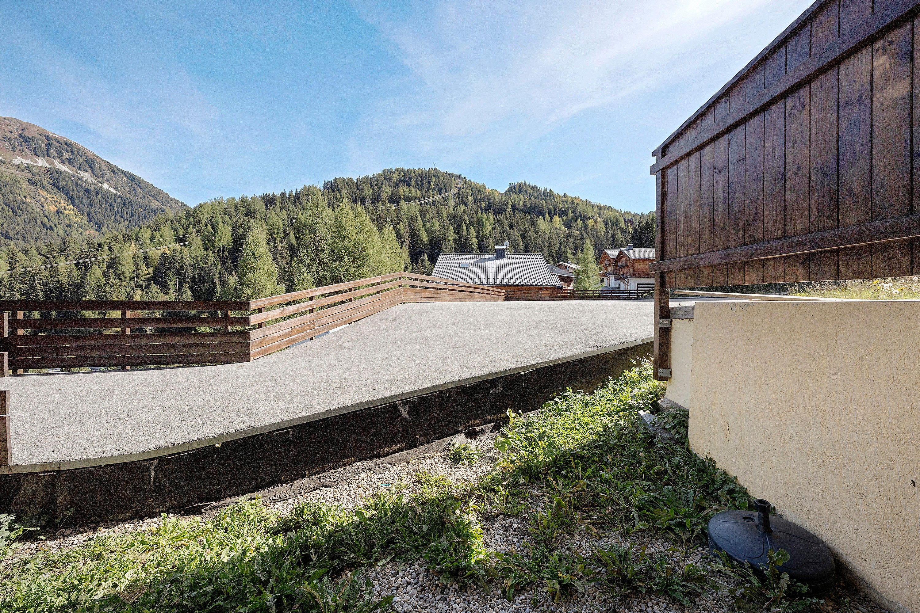 A stable with a wooden fence, a gravel path, and a mountain backdrop.