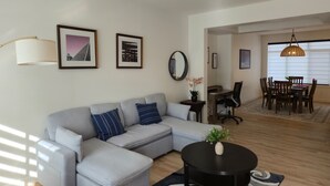 Ein Wohnzimmer mit Sofa, Couchtisch, Essbereich mit Tisch und Stühlen sowie einem Flur, der in einen weiteren Raum führt.