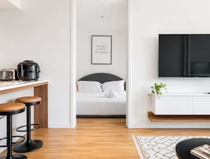 A modern kitchen with a coffee maker, toaster, and bar stools. A framed quote is on the wall, and a bed is visible in the background. - 2BR Stay in Fortitude Valley w/ pool and gym (Brisbane)