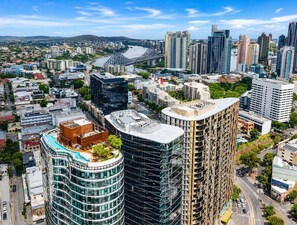 Une vue urbaine avec des immeubles modernes de grande hauteur, un bâtiment remarquable à la forme incurvée surmonté d’un jardin sur le toit, et un pont en arrière-plan.
